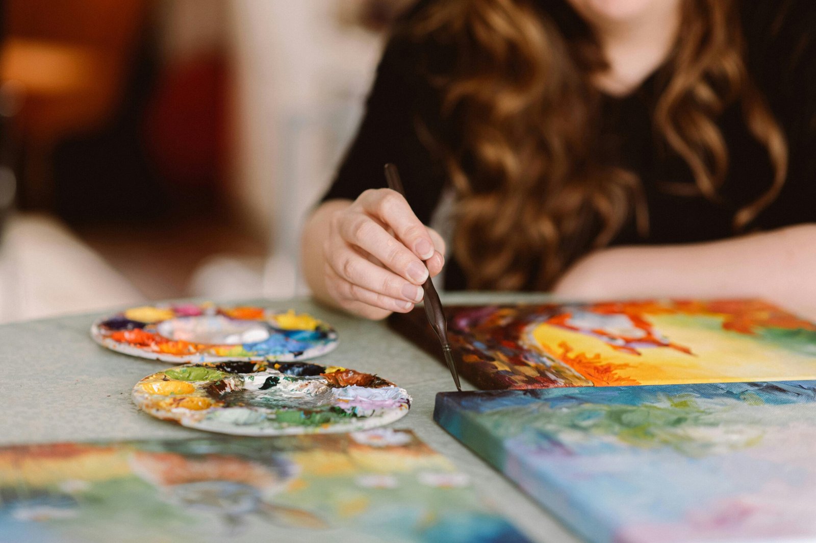 Woman creating art with colorful paint palettes and brushes in a sunlit studio.